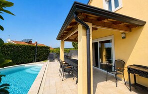 Zona de piscina con terraza techada, mobiliario exterior y una parrilla.