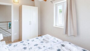 Ein Schlafzimmer mit Bett, Schrank, einem fenster mit Vorhängen und einer Tür zu einem anderen Raum.