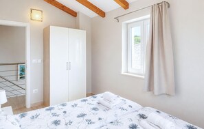 Ein Schlafzimmer mit Bett, Schrank, einem fenster mit Vorhängen und einer Tür zu einem anderen Raum.