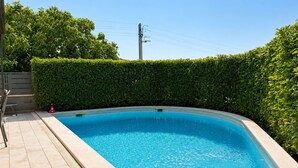 Ein rechteckiger Swimmingpool mit einer gefliesten Terrasse, umgeben von einer ordentlich geschnittenen Hecke.
