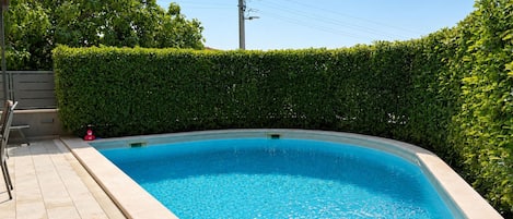 Une piscine rectangulaire avec une terrasse carrelée, entourée d’un arbuste taillé avec soin.