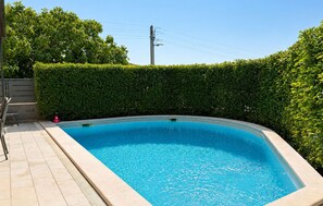 Ein rechteckiger Swimmingpool mit einer gefliesten Terrasse, umgeben von einer ordentlich geschnittenen Hecke.