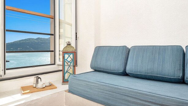 A room with a window overlooking a body of water and hills, a blue sofa, a small table with a kettle and cups, and a decorative lantern. - [FinestraNelBorgo] 5Terre-Portovenere-Seaview (Porto Venere)