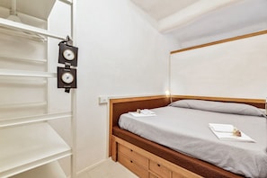 Ein Schlafzimmer mit einem hölzernen Bett, einer grauen Matratze und einer weißen Wand.