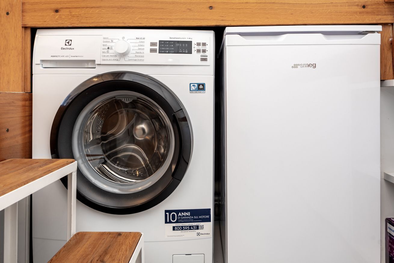 A compact washer and dryer unit with a wooden shelf and a sign indicating a 10-year warranty.