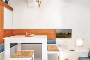 Ein heller Essbereich mit einer Wand aus Holzvertäfelung, einem Tisch mit Obstschale und einem an der Wand montierten Fernseher.