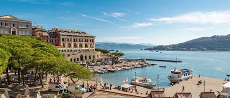 A coastal town with historic buildings, a marina, and a view of the sea and mountains.