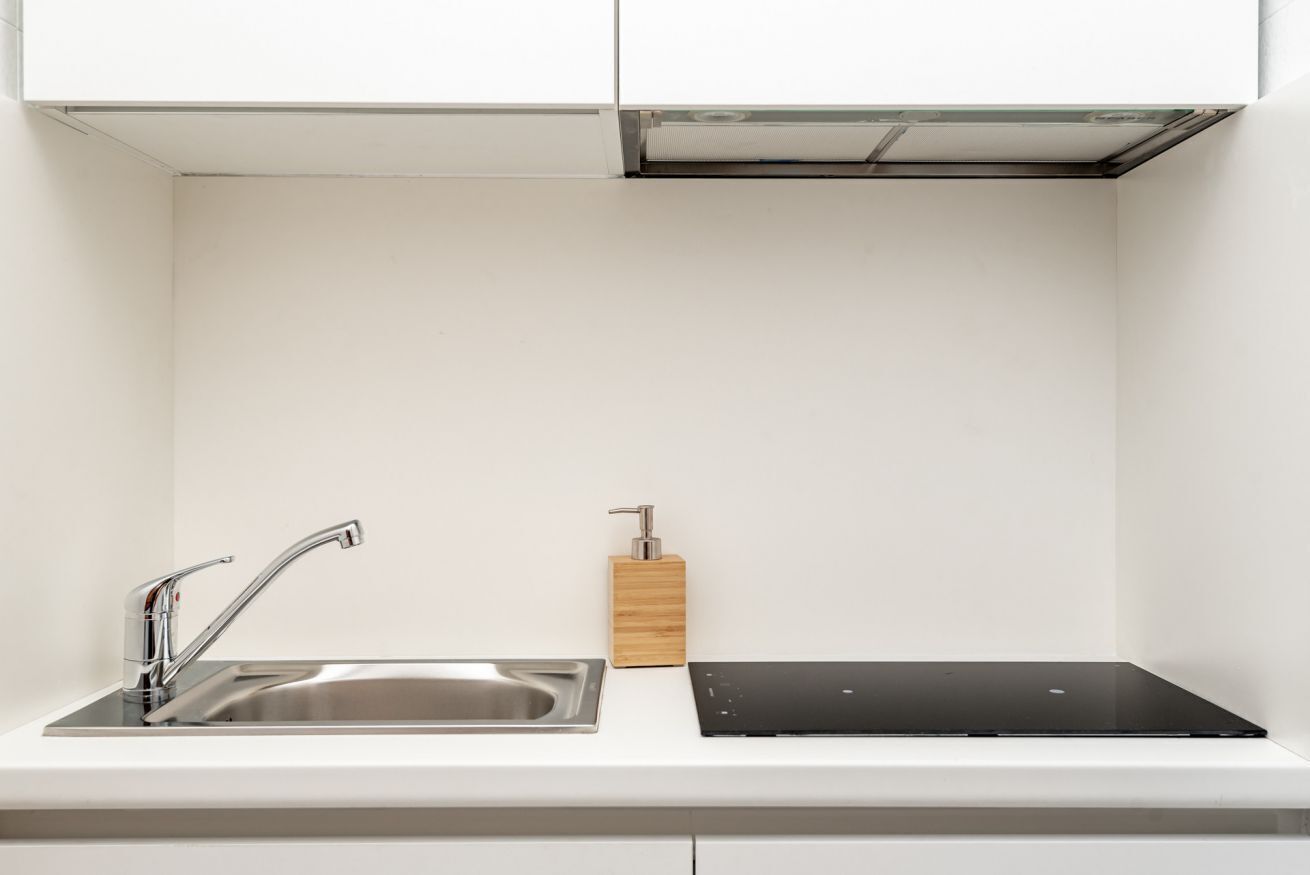 Una cucina moderna con un lavello in acciaio inossidabile, un piano di lavoro nero e un dispenser per sapone in legno.