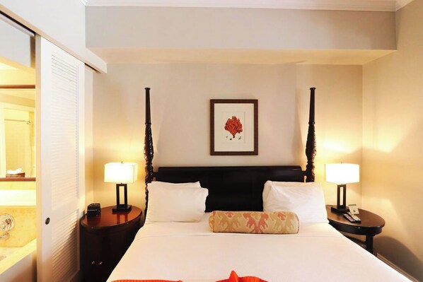 A hotel room with a bed, two bedside tables, a nightstand, a framed picture on the wall, and a window.