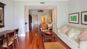 A spacious living room with a wooden floor, a sofa set, a dining table with chairs, and a ceiling fan.