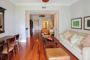 A spacious living room with a wooden floor, a sofa set, a dining table with chairs, and a ceiling fan.