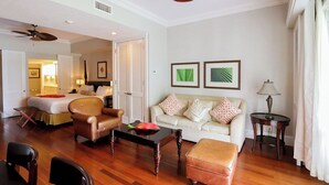 A hotel room with a living area featuring a sofa, armchairs, a coffee table, and a wooden floor.