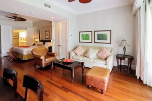 A hotel room with a living area featuring a sofa, armchairs, a coffee table, and a wooden floor.