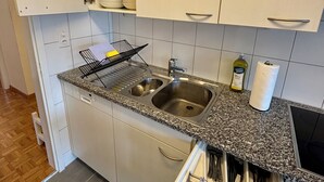Cocina con alacenas blancas, encimera de granito, pileta doble y escurreplatos.