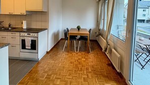 Una cocina moderna con armarios blancos, horno empotrado y comedor con suelo de madera en espiga.