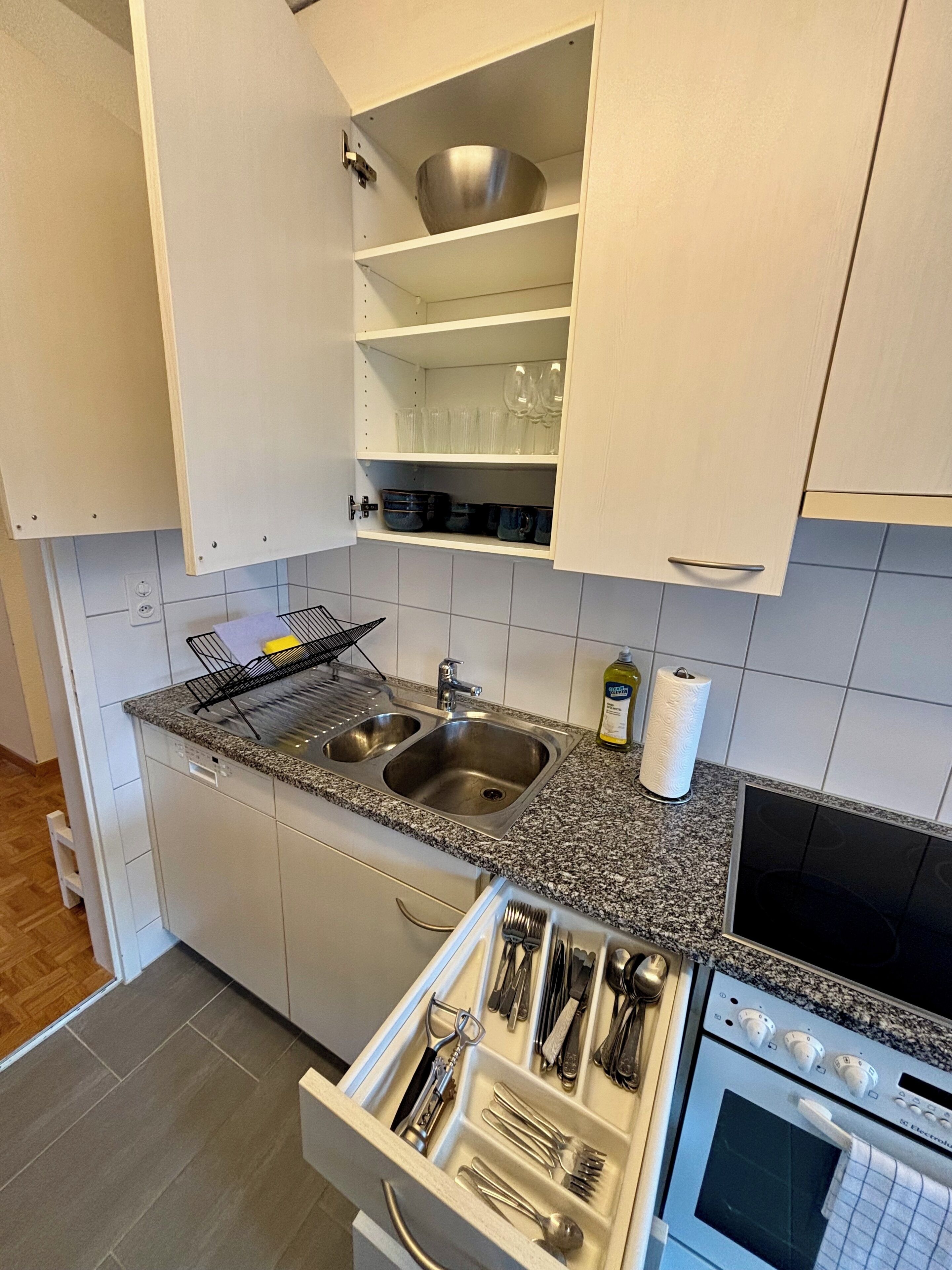Een keuken met witte kasten, een granieten aanrecht, een dubbele spoelbak en een oven.
