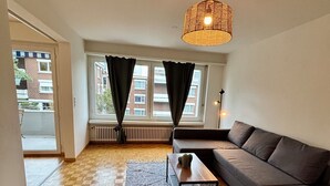 Una sala moderna con un sofá, una mesa de centro, una silla, un tapete estampado y una lámpara colgante.