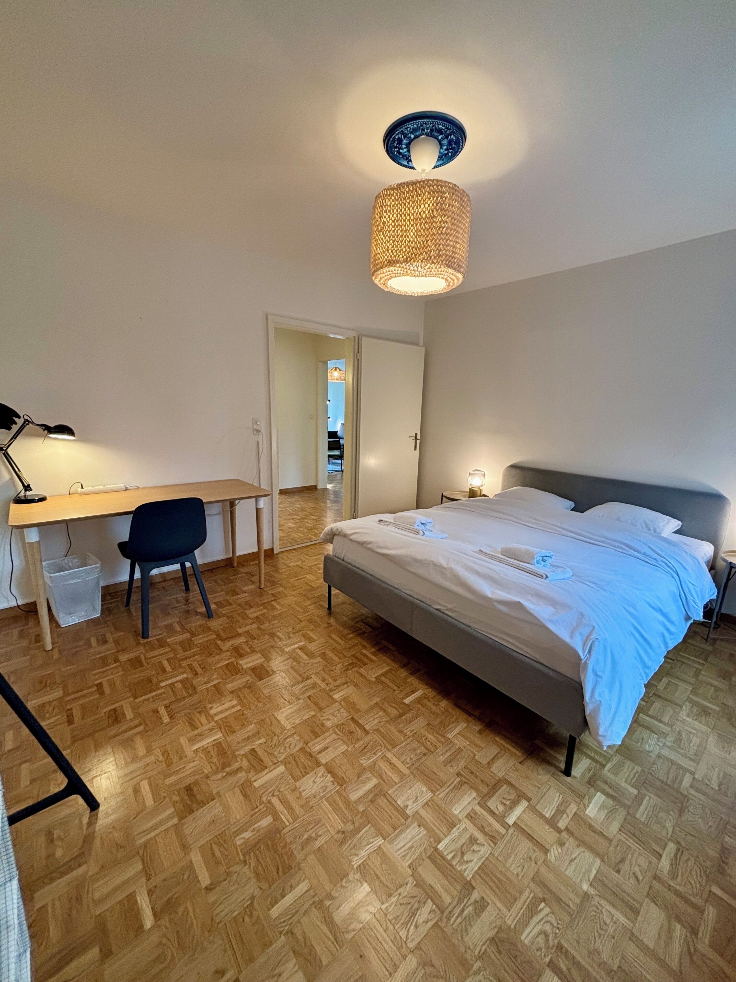 Un dormitorio con una cama, un escritorio y una silla. Hay una puerta que da a otra habitación.