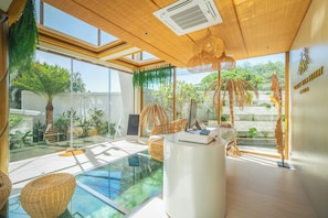 A modern interior with a glass pool, indoor plants, and a computer on a desk. - Westkey Luxury Villa (Kathu)
