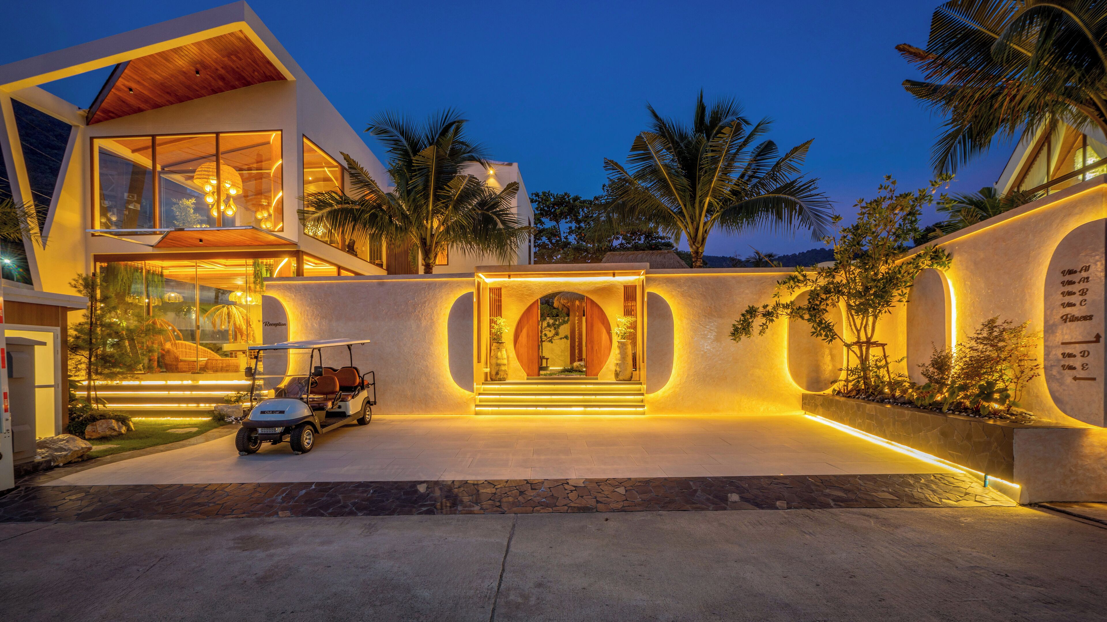 A modern house with a large glass facade, a golf cart, and a well-lit entrance.