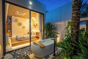Interior moderno com uma banheira grande, ambiente bem iluminado e uma cama visível.