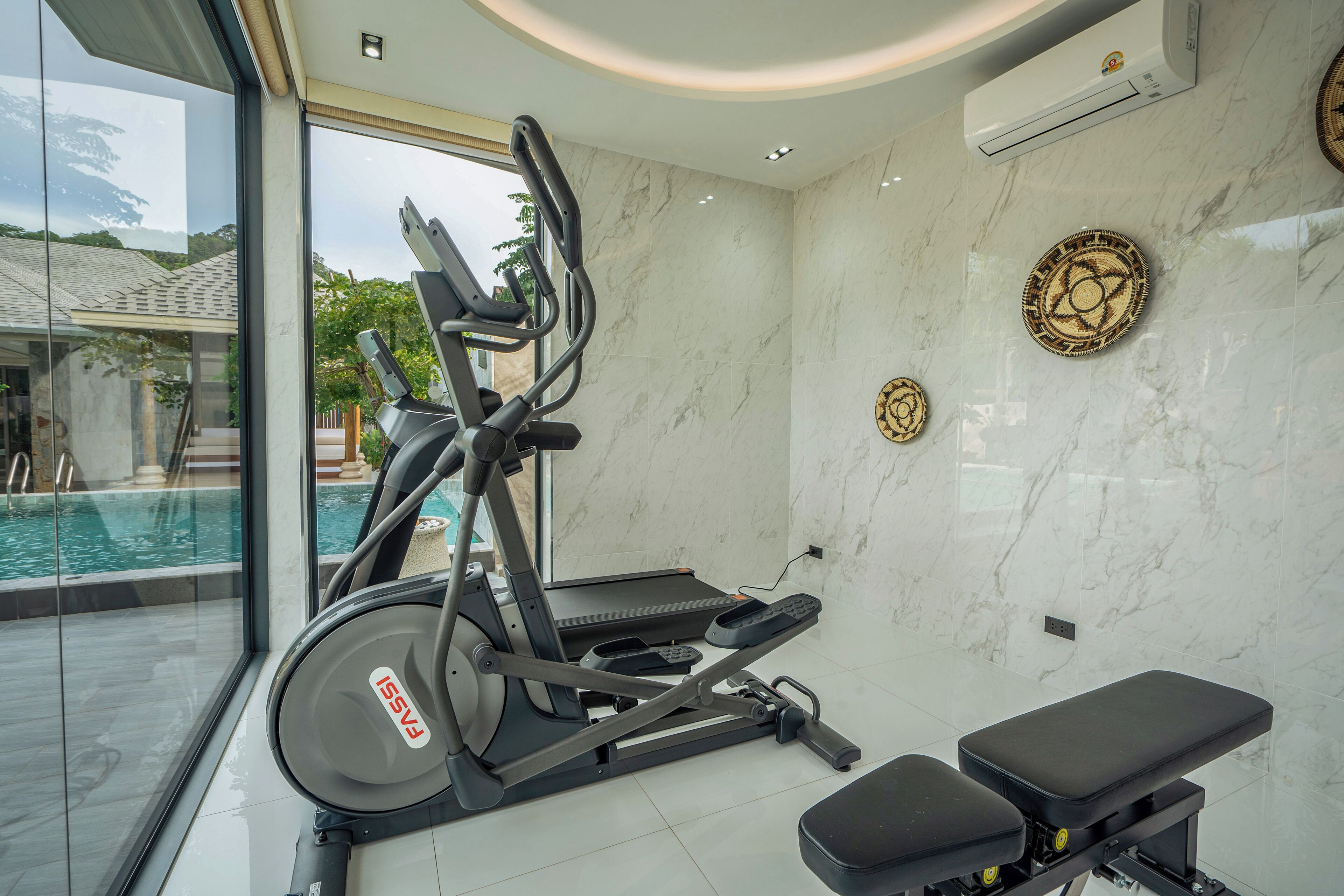 Academia com equipamentos de exercício, um banco e vista para uma piscina.