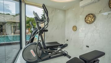 Academia com equipamentos de exercício, um banco e vista para uma piscina.