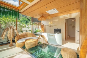 Uma área de recepção com balcão, móveis de vime, piscina de vidro e vista para o verde lá fora.