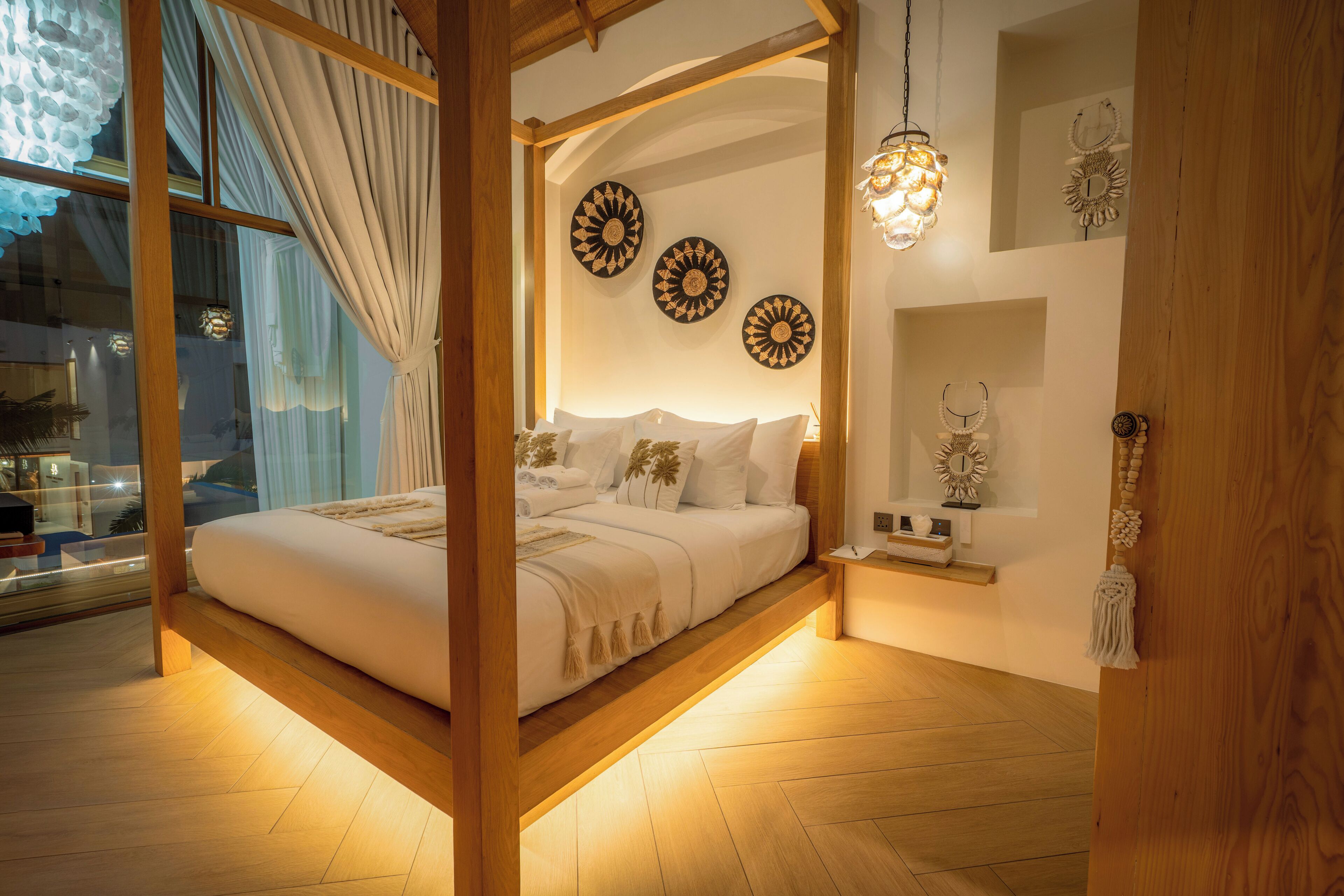 Quarto com cama de dossel, vigas de madeira, uma grande janela com cortinas e decoração nas paredes.