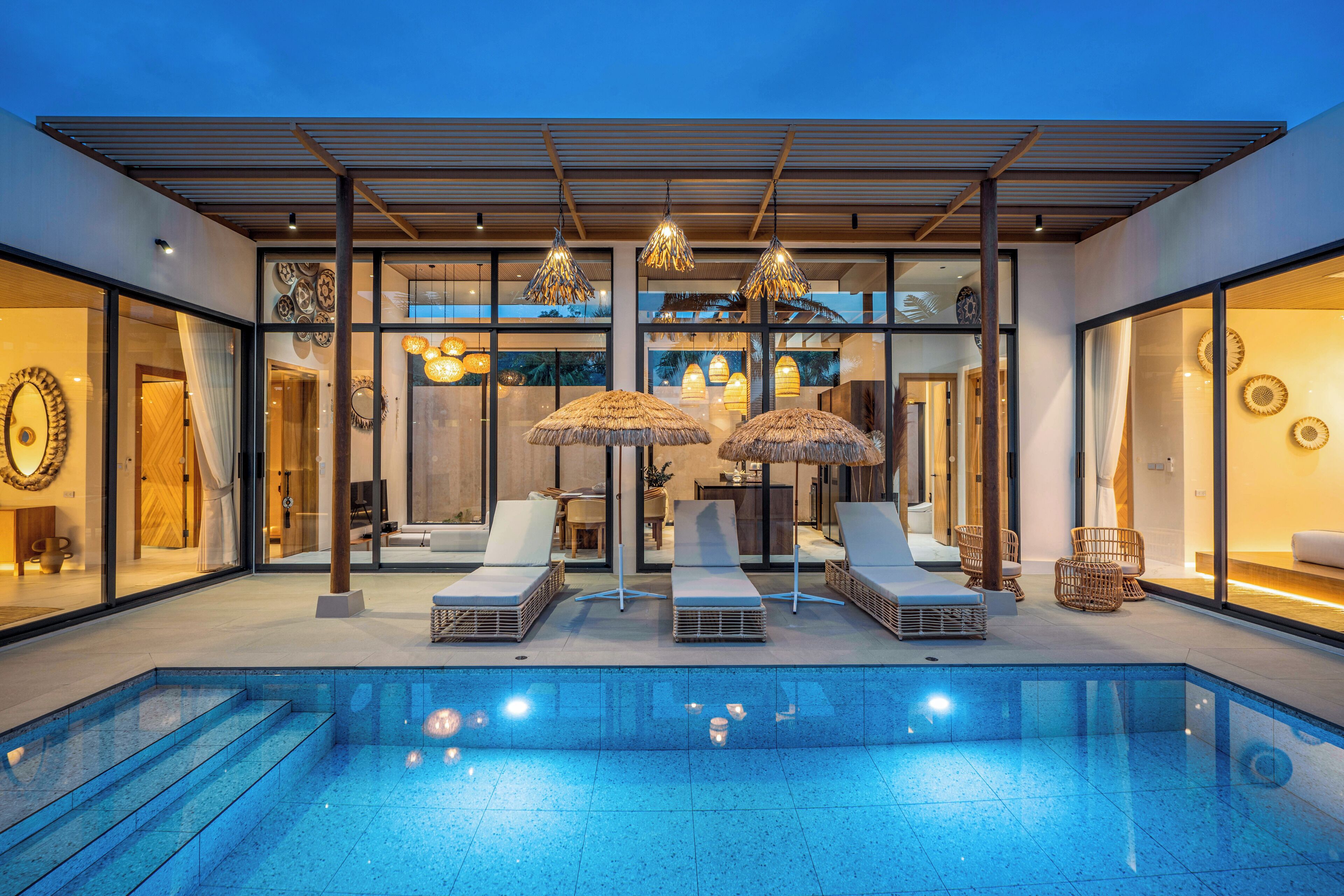 A modern outdoor pool area with lounge chairs and umbrellas, surrounded by glass walls and a wooden pergola.