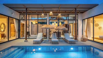 A modern outdoor pool area with lounge chairs and umbrellas, surrounded by glass walls and a wooden pergola.