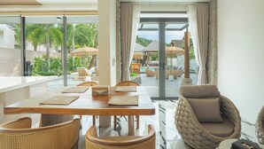 Uma sala de jantar moderna com mesa de madeira, cadeiras de fibra natural e vista para uma piscina e área externa.
