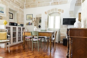 A room with a wooden herringbone floor, a dining table with chairs, a television mounted on the wall, and a stone wall. - Terrazza Calipso by Wonderful Italy (Ostuni)