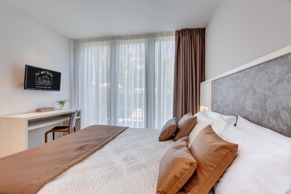 A hotel room with a bed, a desk, and a large window with curtains.