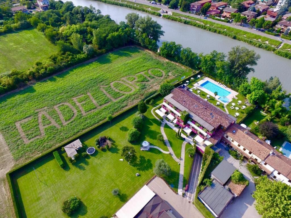 Vista aerea di una proprietà con piscina, campo da tennis e un ampio prato verde con la scritta 'EADELERTO'.