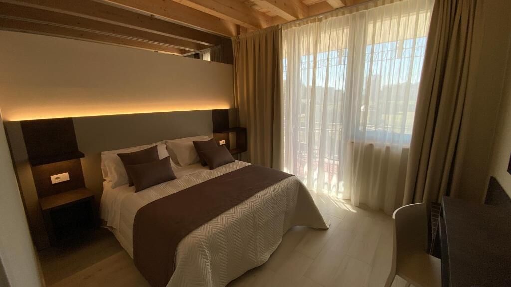 Un dormitorio moderno con una cama grande, mesitas de noche y vistas al exterior a través de cortinas translúcidas.