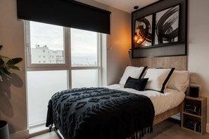 Ein Schlafzimmer mit Bett, einem Fenster, Blick auf die Stadt und Kunstwerken an der Wand.
