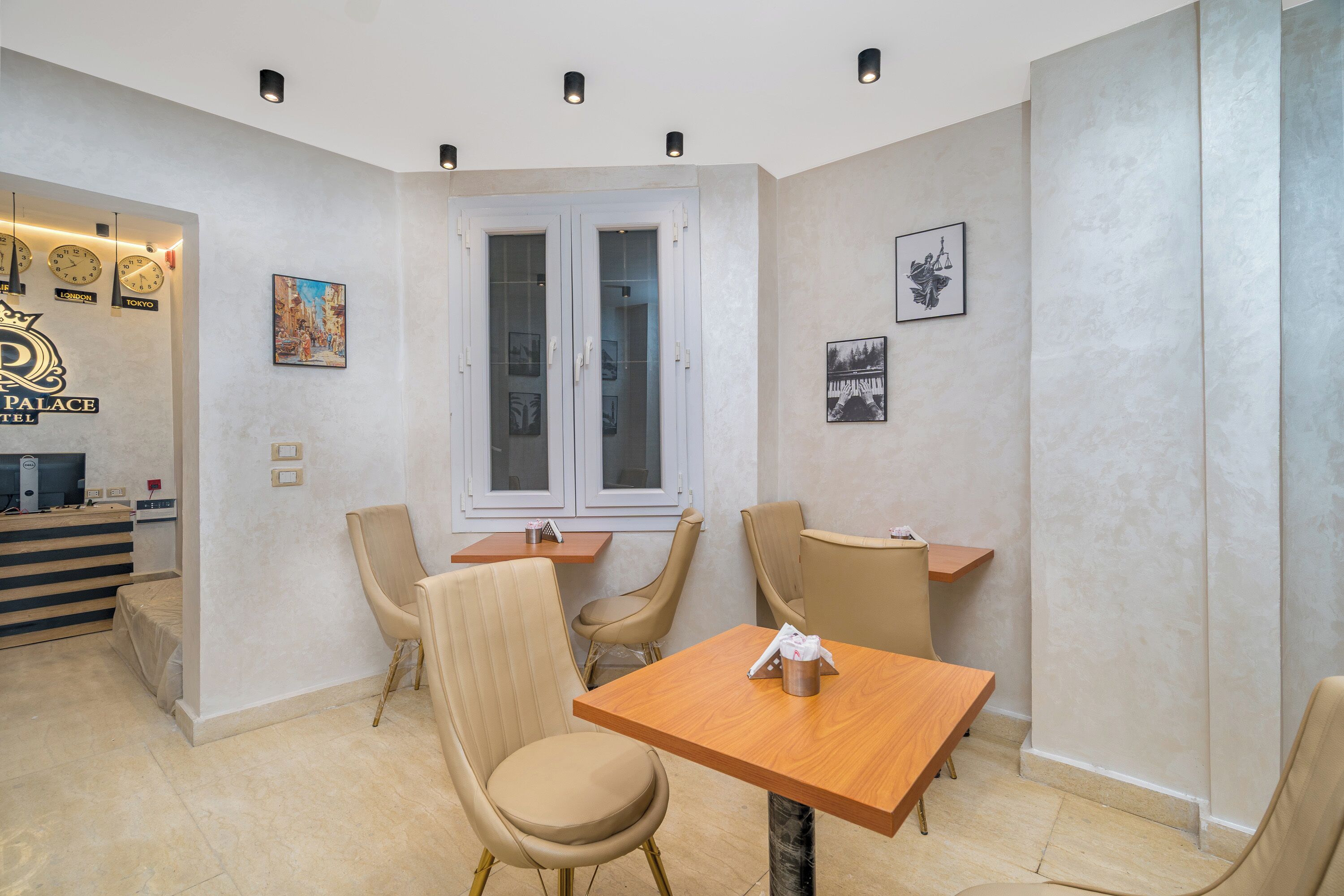 Habitación de hotel con una mesa de madera, sillas color beige, un escritorio con computadora y obras de arte en las paredes.