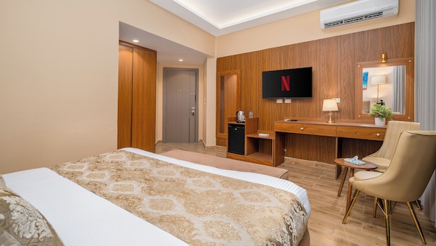Quarto de hotel com uma cama grande, uma escrivaninha, uma cadeira, uma televisão e um ar condicionado.