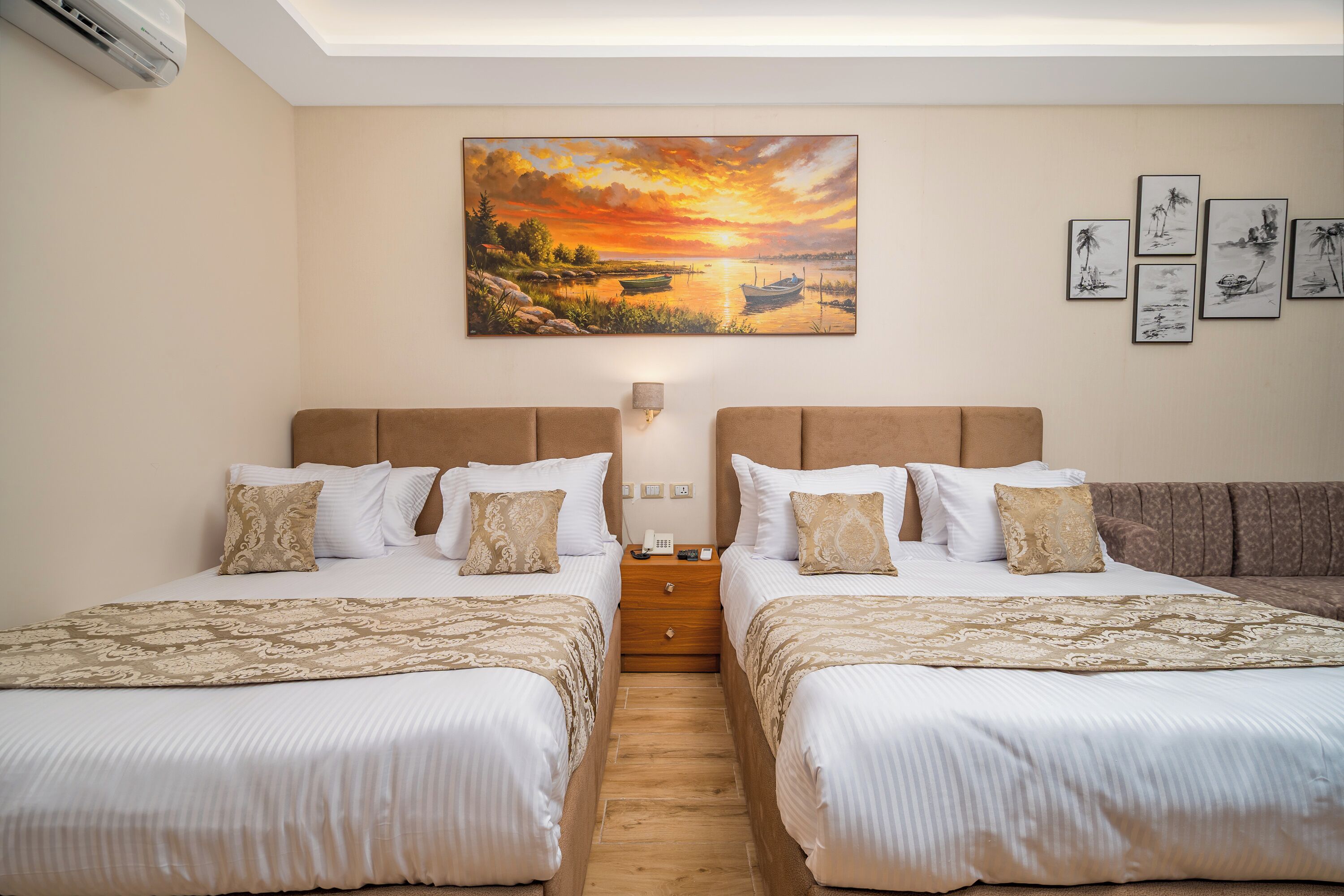 Une chambre d’hôtel avec deux lits, un tableau représentant un coucher de soleil et plusieurs photos encadrées accrochées au mur.