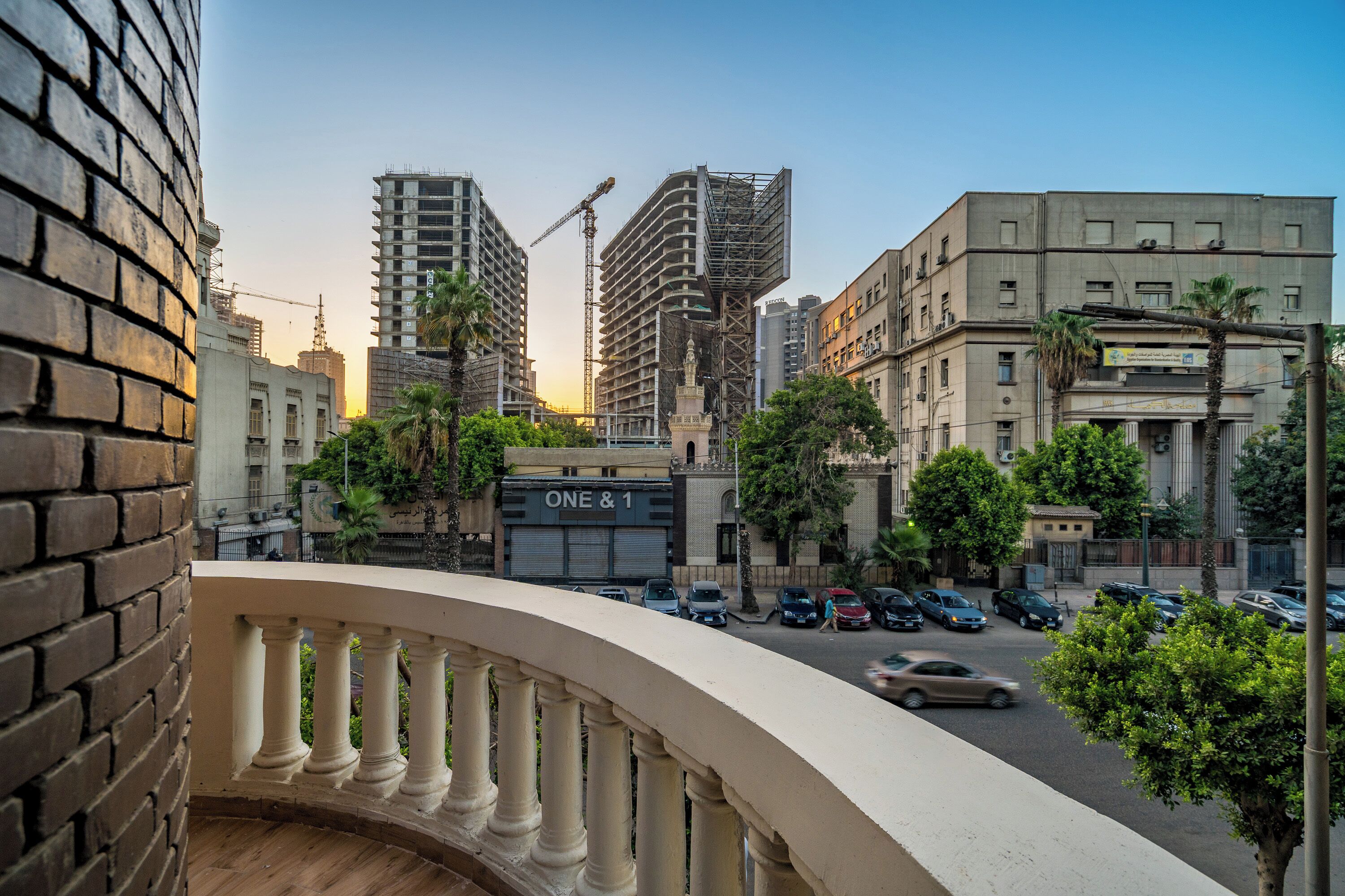 A cityscape with modern buildings, a construction crane, and parked cars.