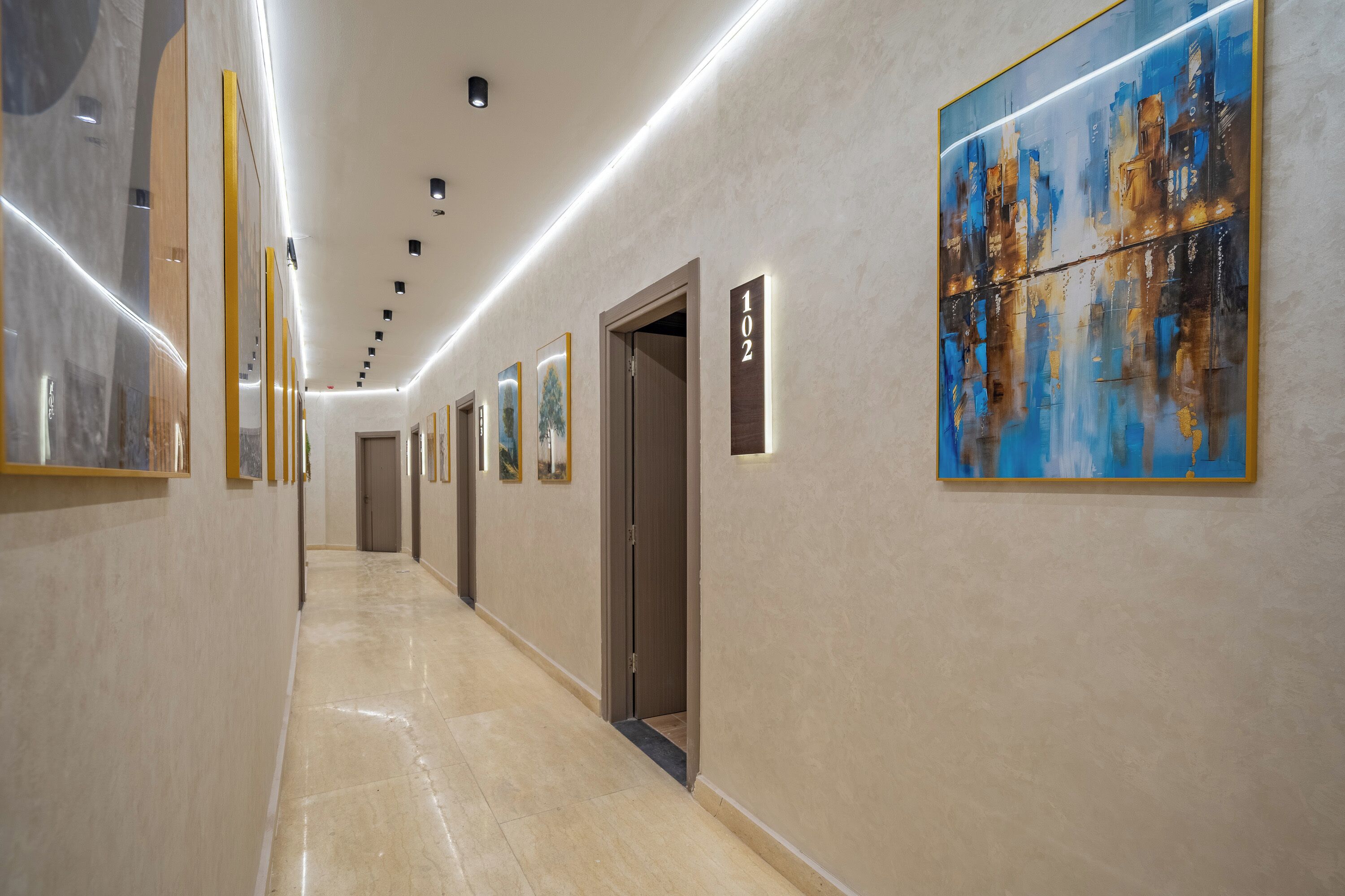 Un couloir d’hôtel avec des œuvres d’art accrochées aux murs, un panneau indiquant le numéro de la chambre et une porte.