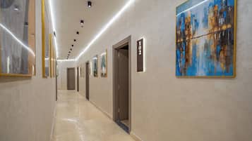 Un couloir d’hôtel avec des œuvres d’art accrochées aux murs, un panneau indiquant le numéro de la chambre et une porte.