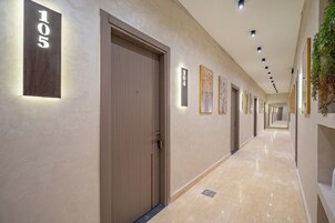 Un couloir d’hôtel avec des portes numérotées 105 et 104, un sol en marbre et des luminaires encastrés au plafond.