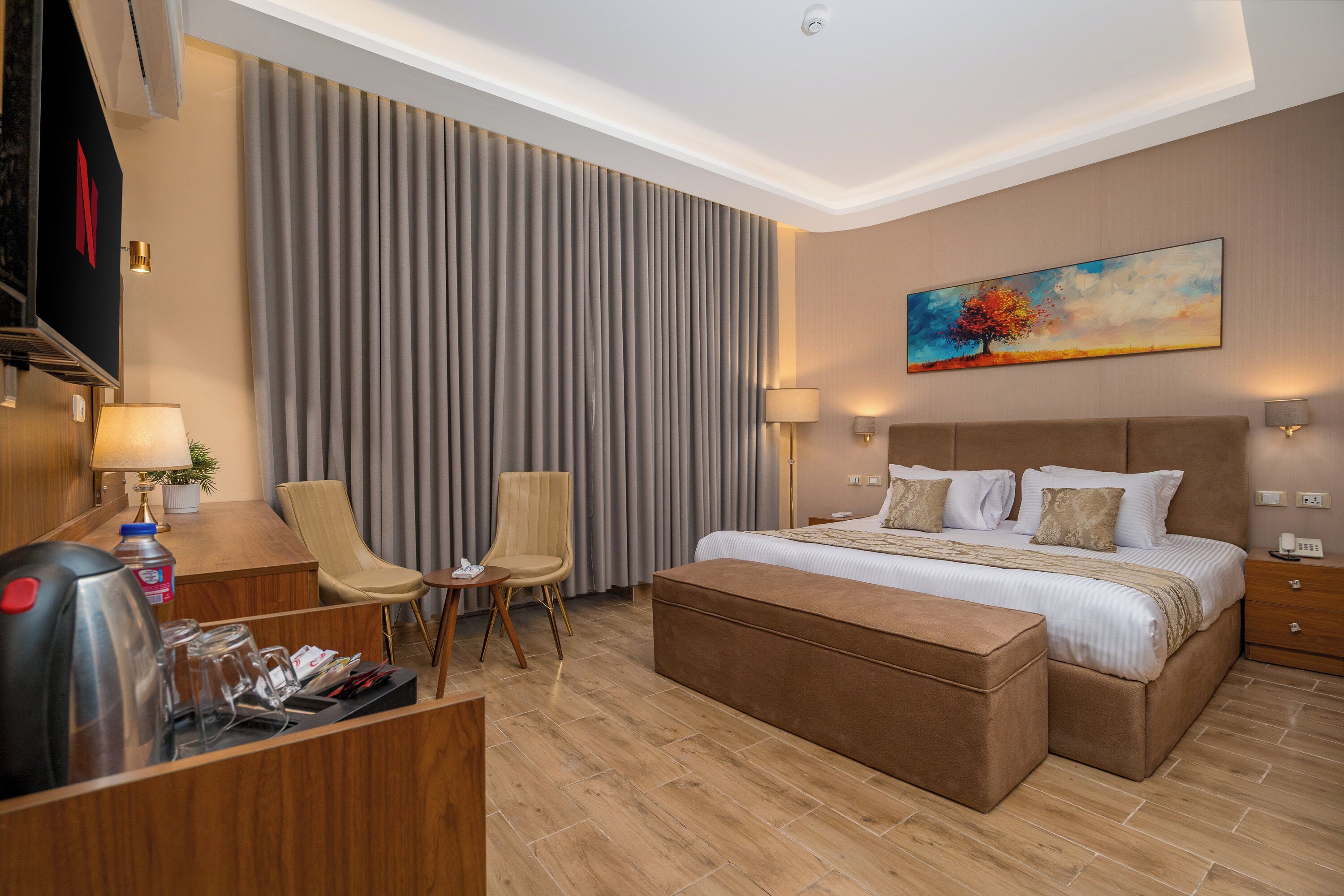 A hotel room with a bed, two chairs, a desk, and a painting on the wall.