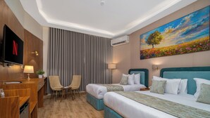 Quarto de hotel com uma cama, duas mesas de cabeceira, uma escrivaninha com cadeira, uma televisão e um quadro na parede.