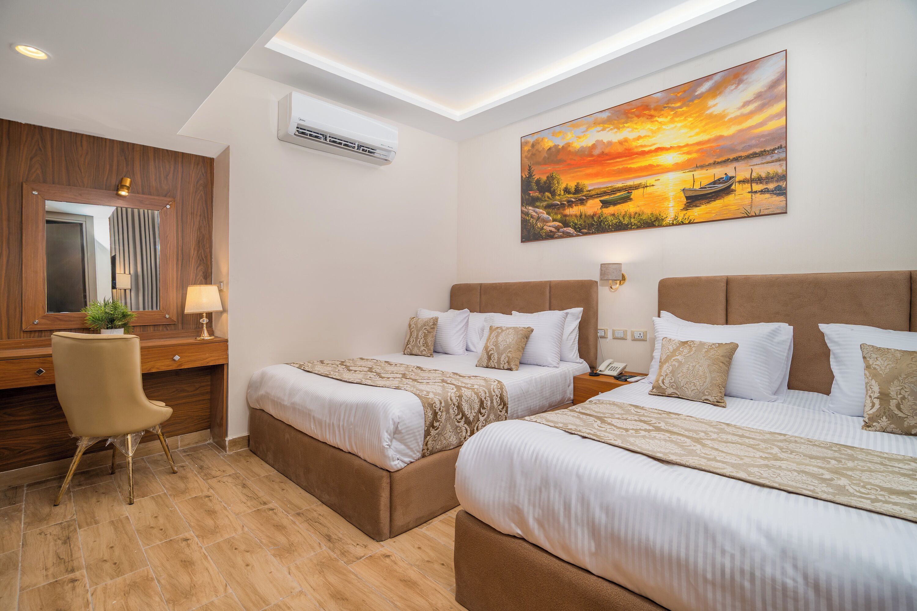 Una habitación de hotel con dos camas, un escritorio, una silla, un aire acondicionado, un cuadro y un espejo.