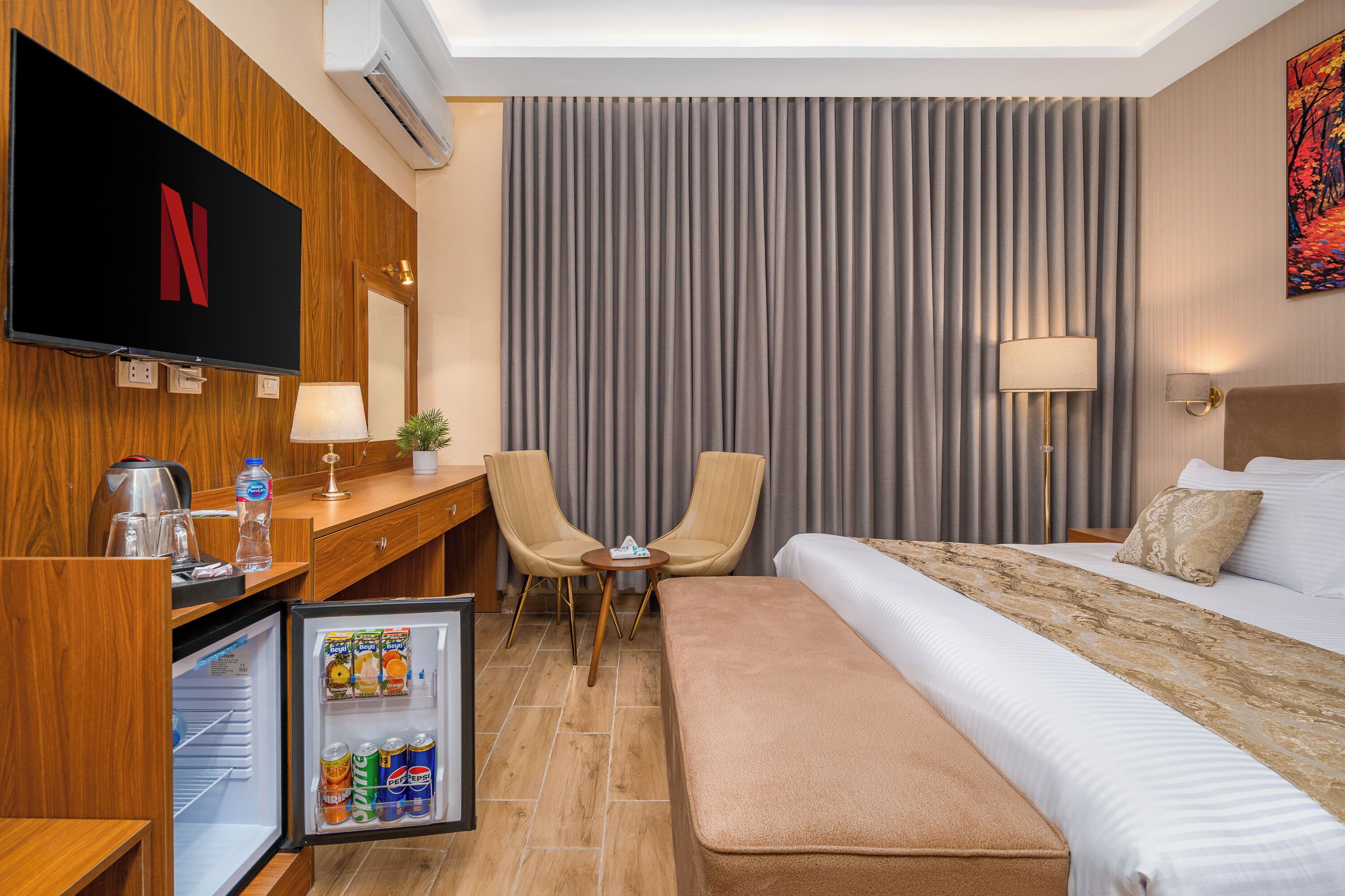 A hotel room with a bed, a desk with a computer, a television, a refrigerator, and a window with curtains.