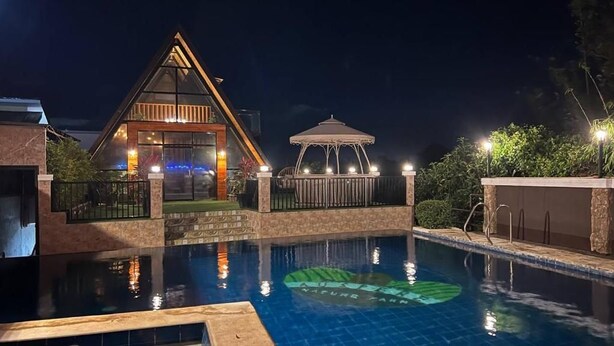 Ein Hotel bei Nacht mit Schwimmbad, Gazebo und einem Gebäude mit einem dreieckigen Dach.