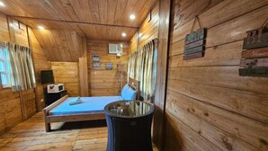 Ein Zimmer in einer Holzhütte mit einem Bett, einem kleinen Tisch und einem Mülleimer.